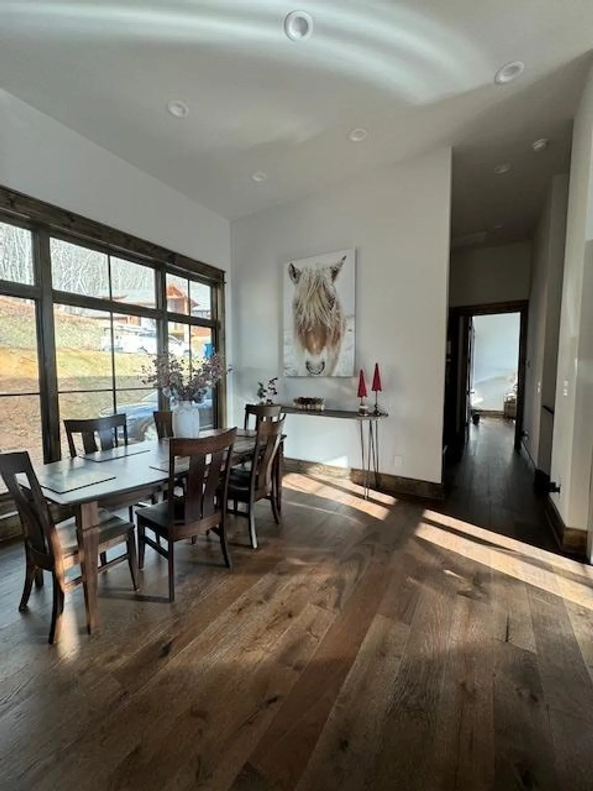 A cozy dining area with a wooden table set beside large windows, featuring decorative candles and horse artwork. The room exudes warmth and is ideal for intimate dinners, celebrations, or heartfelt conversations with friends.