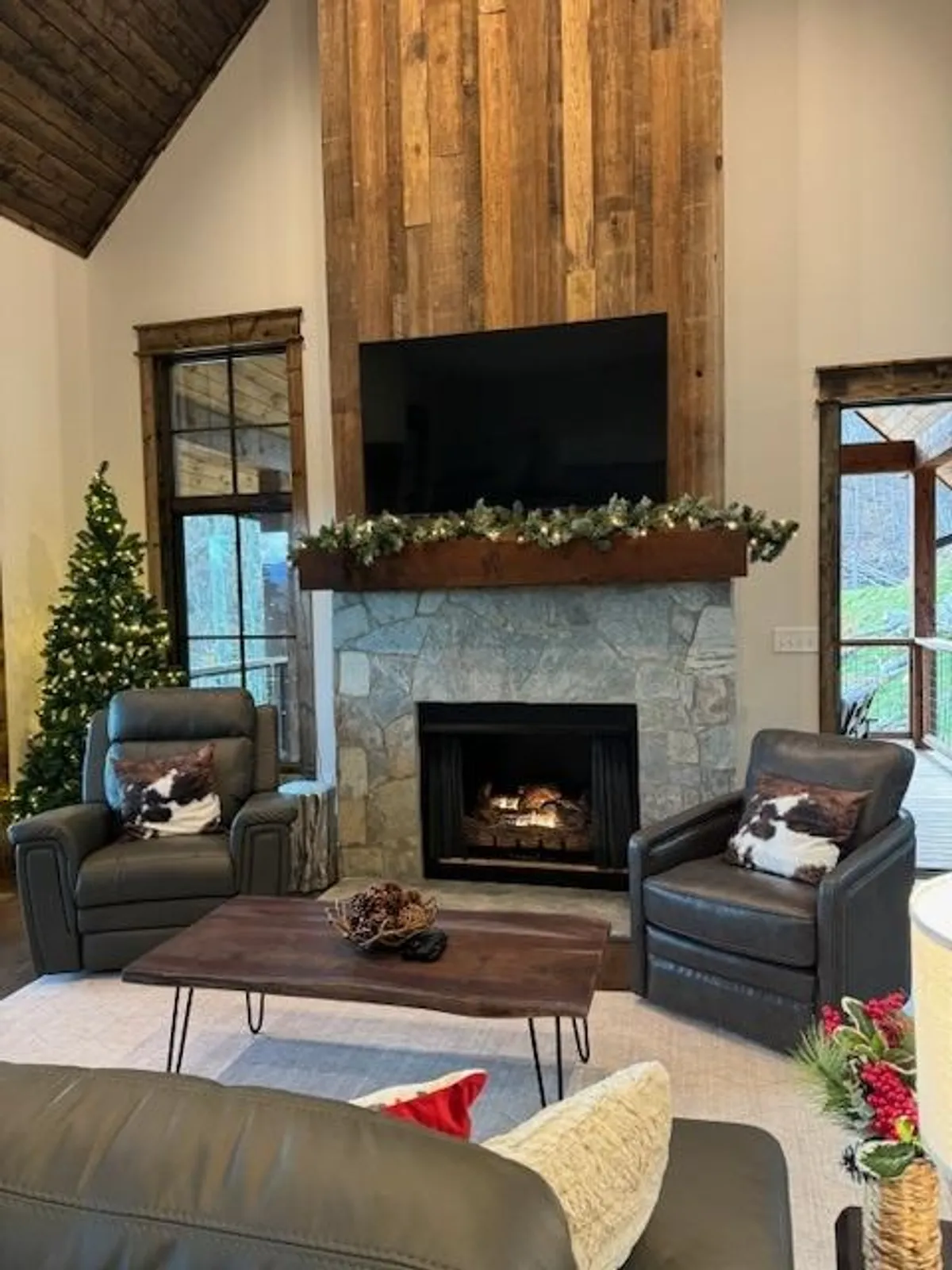 A den scene centered on a fireplace, wood-paneled walls, comfortable seating, and festive touches like a Christmas tree. The space exudes warmth and an inviting atmosphere ideal for cozy gatherings and movie nights.