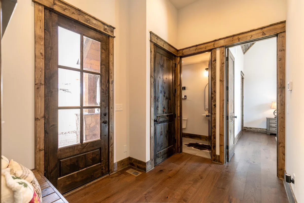 A welcoming entryway with warm wooden doors, wood flooring, and soft lighting, suggesting the threshold between the outside and the home. The scene hints at guests or residents entering after a day of exploration.