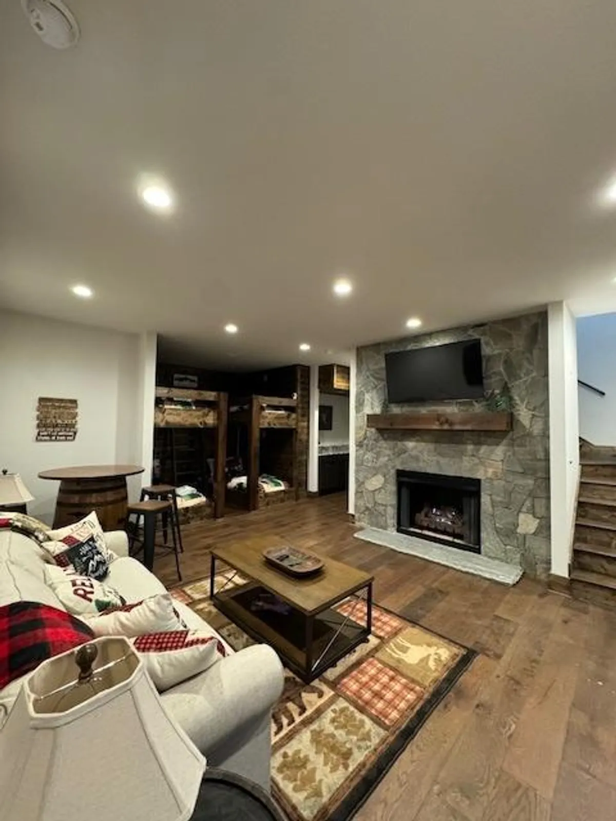 This image showcases a welcoming den featuring a warm fireplace, a cozy sofa, coffee table, and visible bunk beds in the background. The space feels ideal for group gatherings, movie nights, and play, with soft lighting and inviting furnishings enhancing the atmosphere.