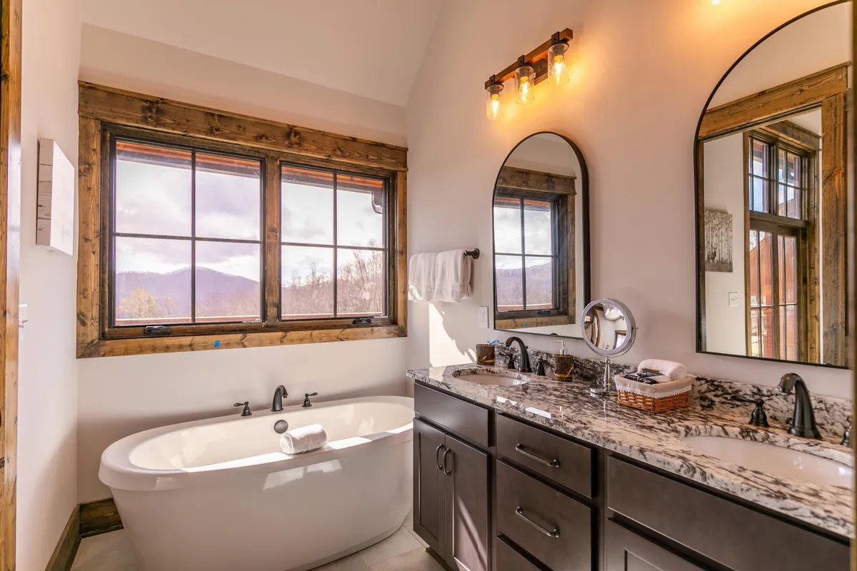 A luxurious bathroom with a freestanding soaking tub positioned beside large windows with mountain views, complemented by a double granite vanity, creating an oasis of relaxation and elegance.