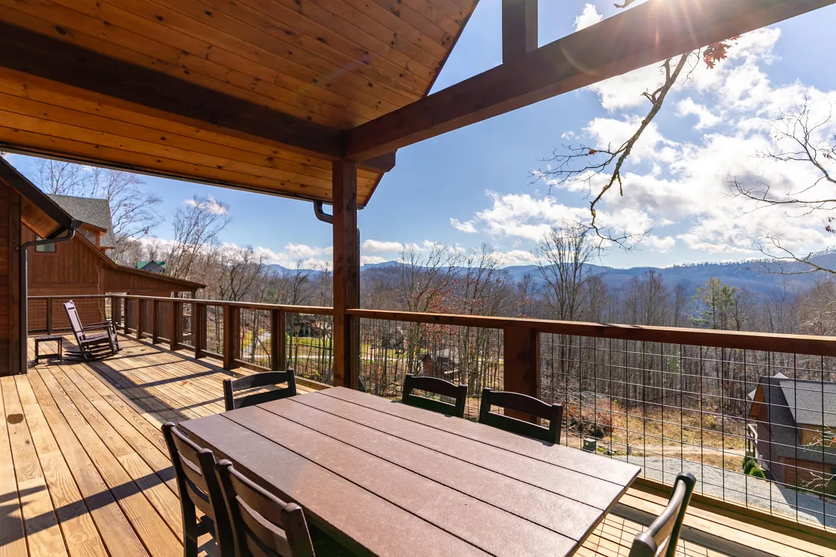 A spacious wooden deck set against a backdrop of scenic mountain views features an outdoor dining table, ideal for meals beneath the open sky. The setting is inviting for gatherings, with room for family or friends to enjoy both the fresh air and the breathtaking landscape.